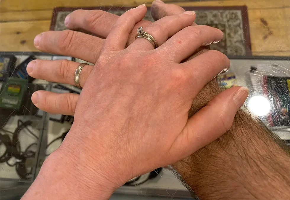 Wife's hand atop husband's hand with wedding rings visible.